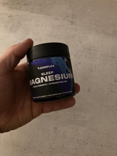 Customer holding a black jar of Complex Sleep Magnesium against a neutral background.