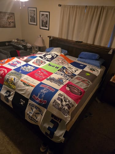 Customer's colorful Premium T Shirt Quilt made from various sports tees, spread across a bed in a bedroom.