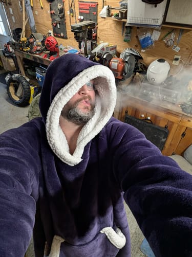 Reviewer in a workshop exhales smoke after using the World of Cats Beaker Glass Bong.
