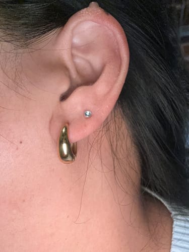 Close-up of a reviewer's ear wearing the gold Mini Drop Huggies earring.