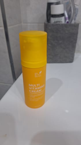 Un cliente mostra la Multi Vitamin Cream nel suo flacone giallo su un lavandino del bagno.