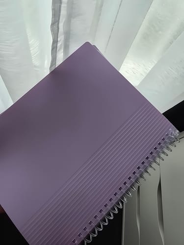 Un client montre le protège-documents OXFORD A5 en plastique violet pastel avec sa reliure à spirale transparente.