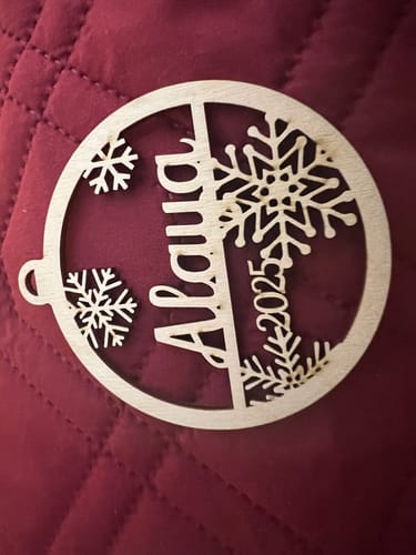 Customer's personalized birch wood ornament with the name "Alaiia" and "2025" laser-cut into a snowflake design.