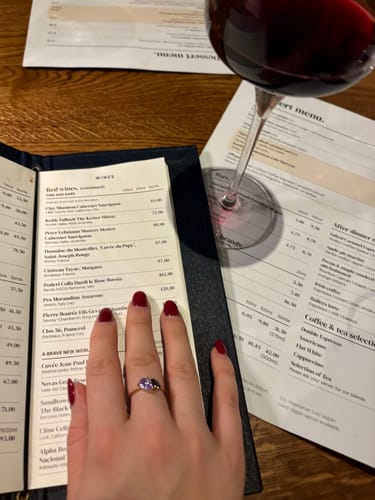 Reviewer's hand wearing the gold Leesha Birthstone Ring with purple and blue stones at a restaurant.