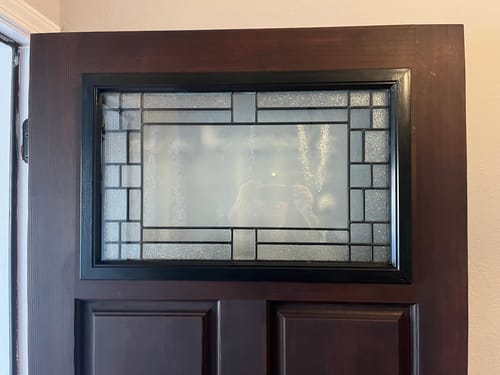 Close-up of a reviewer's Portland Glass and Frame Kit installed in a dark brown door showing the intricate glass design.
