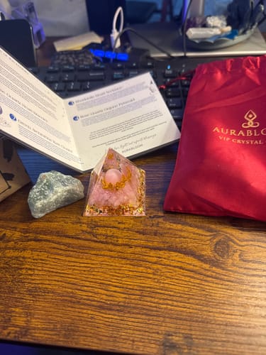 Customer's AuraBloom Subscription Box showing a pink Rose Quartz Pyramid and a green Aventurine stone on a wooden desk.