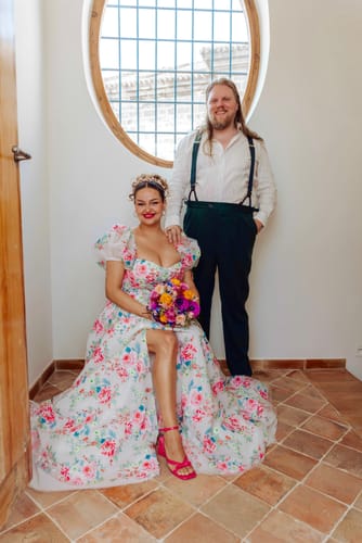 Reviewer seated indoors wearing the floral Enchanted Elegance Rose Gown, showing its puff sleeves and leg slit.