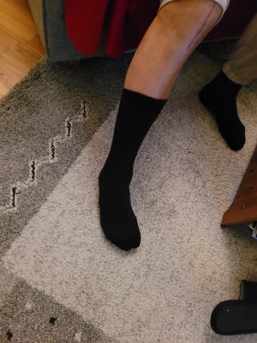 En kund som visar sina svarta Diasocks Komfortstrumpor på fötterna inomhus.