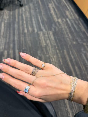 Customer's hand showing the Pia Ring on the index finger, styled with other rings and layered bracelets.
