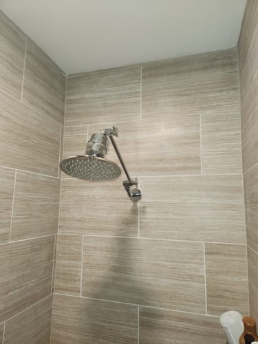 Customer's shower filter installed with a chrome adjustable arm and rain shower head in a tiled shower.