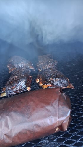 Customer's USDA Choice Bone-In Short Ribs with a dark crust smoking on a grill grate.