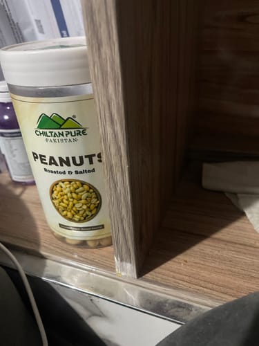 Partial view of a customer's clear jar of roasted and salted peanuts sitting on a wooden surface.