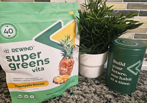 Customer's bag of Rewind Super Greens vita in Pineapple Dream flavor sitting on a kitchen counter next to a canister and plant.