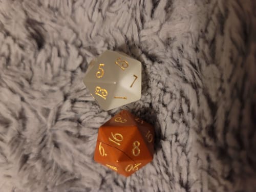 Customer's two Mystery Dice from a blind bag: one translucent white and one orange die on a soft grey surface.