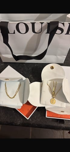 Customer's white gift bag shown behind two open jewelry boxes containing gold necklaces.