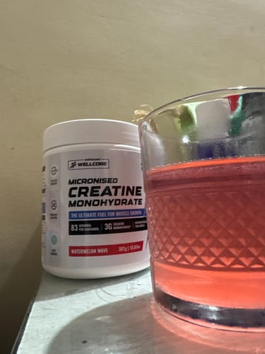 Customer's tub of Wellcore Micronised Creatine Monohydrate next to a glass of the prepared red drink.
