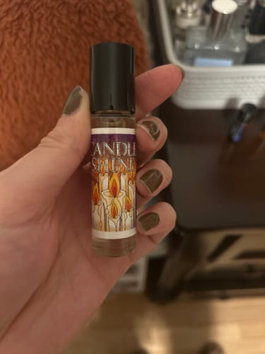 Reviewer holding a small rollerball bottle of Candle Shine, showing the candle-illustrated label.