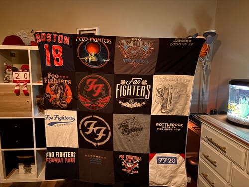 Reviewer displaying their new Premium T Shirt Quilt made from various dark-colored Foo Fighters concert t-shirts.