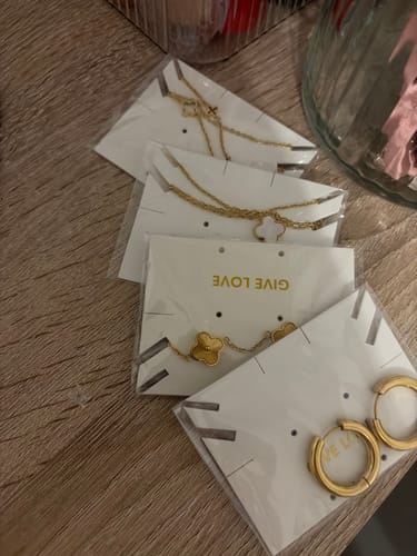 Kunde zeigt die goldenen Glossy Hoops in der Verpackung neben anderem Schmuck auf einem Holztisch.