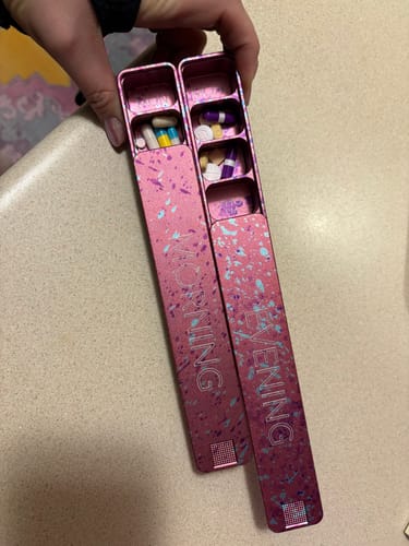 Customer holding the two open sections of the pink Weekly AM-PM Pill Case, with various pills visible inside.