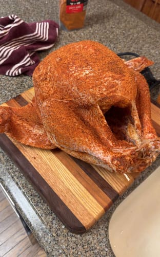 Customer's raw turkey covered in red seasoning from the Turkey Brine Kit on a wooden cutting board.