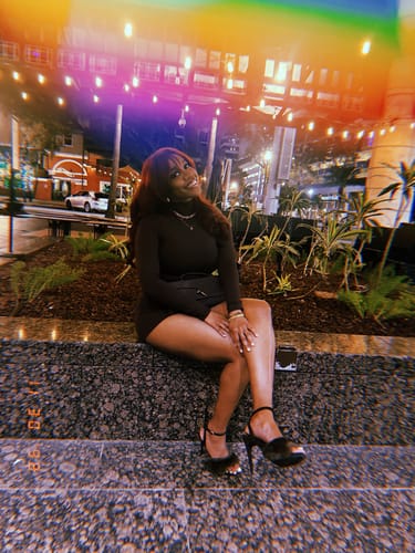 Customer sitting on a ledge outdoors at night wearing the dark Butter Turtleneck Contour Bodysuit.