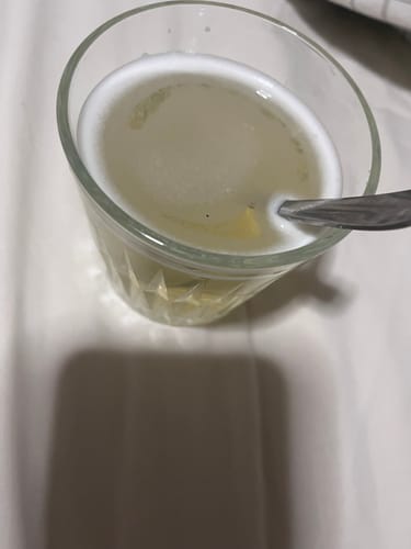 Reviewer stirring a foamy supplement drink in a clear glass with a spoon.
