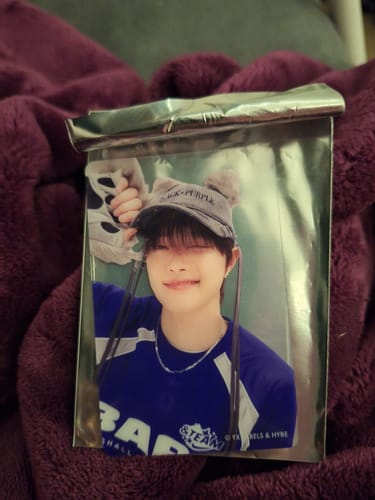 Customer holding a &TEAM Clear Photo Card showing a member in a grey hat, partially in its silver packaging.