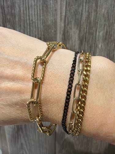 Customer's wrist showing the Statement Rope Paperclip Bracelet layered with three other gold and black bracelets.