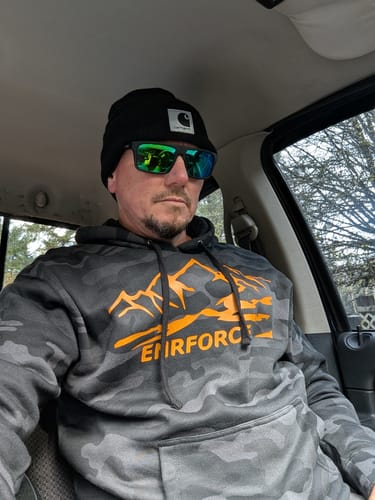 Reviewer sitting in a car wearing the black camo Rocky Camo Hoodie with an orange mountain graphic.