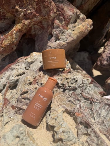 Customer's Accelerating Tanning Oil bottle and a matching product tub resting on large, textured rocks.