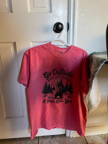 Customer's pink Go Outside T-shirt with a humorous bear graphic hanging on a door.