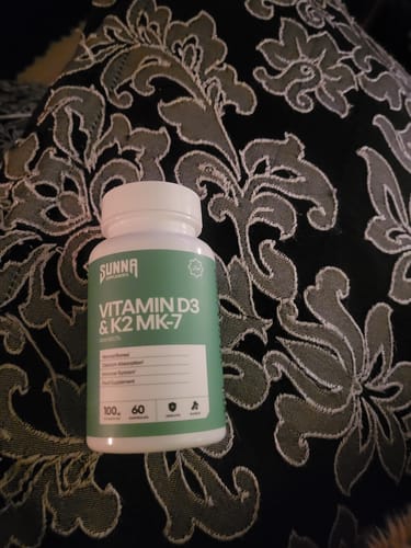 Customer's bottle of Sunna Vitamin D3 & K2 MK-7 supplements resting on a black and grey patterned surface.