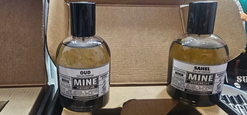 Recensore mostra il flacone di profumo SAHEL accanto a un altro nella scatola di imballaggio.