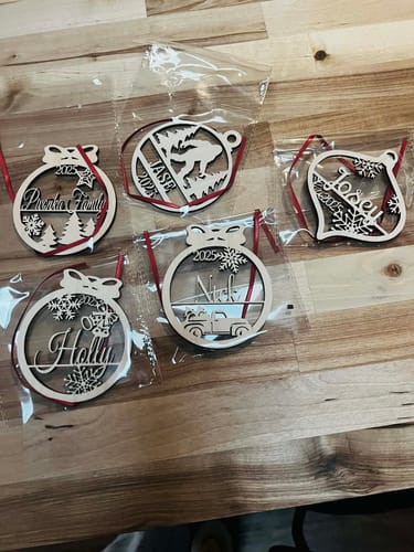 Customer's five personalized wooden Christmas ornaments with different laser-cut designs laid out on a wooden table.