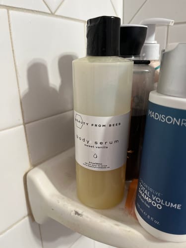 Customer's bottle of Sweet Vanilla Body Serum sitting on a white shower caddy.