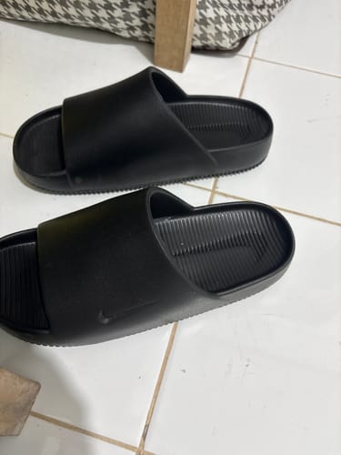 Customer's pair of black Nike Men's Calm Slides on a white tiled floor.