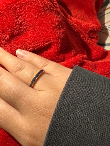 A person wearing the French Cut Sapphire Half Eternity Band in yellow gold against a red, fuzzy background.