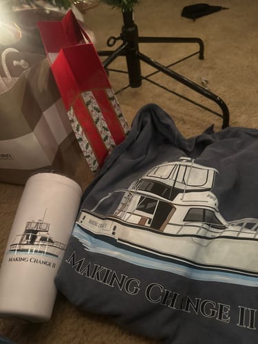 Customer's custom boat artwork printed on a blue t-shirt and a white tumbler, sitting on the floor by a Christmas tree.