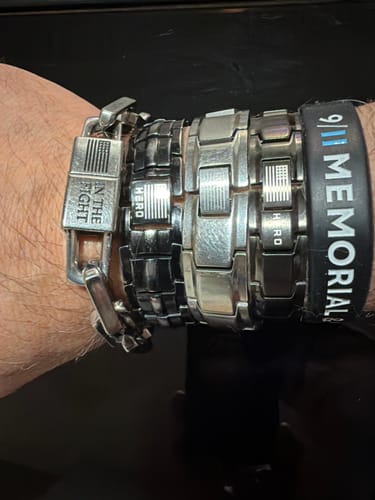 Close-up of a customer's wrist wearing several silver and black Body Armor Titanium Bracelets stacked together.