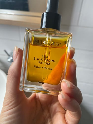 Customer holding a square bottle of the amber-colored Sea Buckthorn Serum.