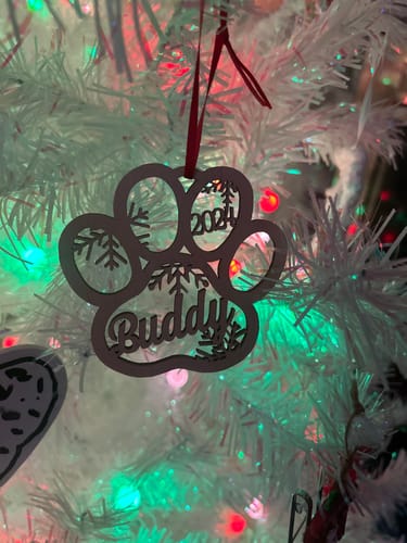 Reviewer's personalized wooden paw print ornament with the name "Buddy" and the year "2024" hanging on a white Christmas tree.