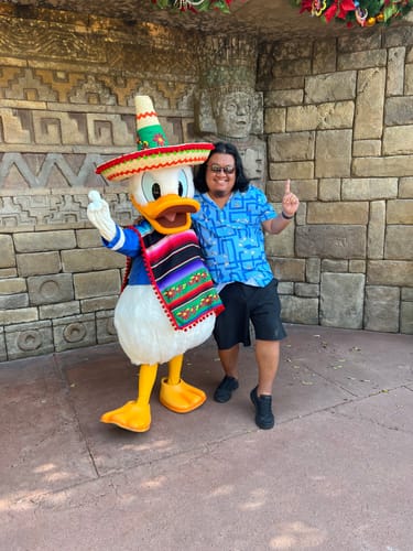 Customer wearing the blue 'Out on a Limb' shirt while posing with Donald Duck at a theme park.