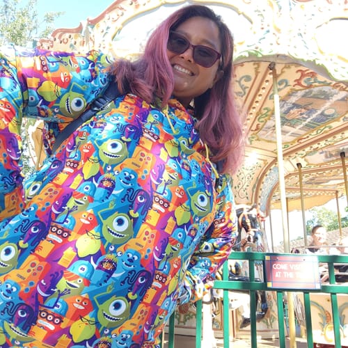 Reviewer smiling in a colorful Monsters, Inc. Performance Hoodie by a carousel.