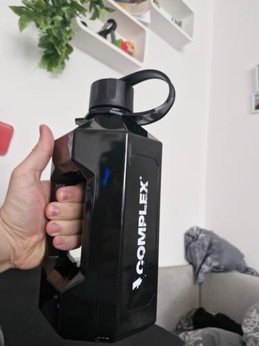 A customer's hand holding the large black Complex XXL Bottle by its integrated side handle.