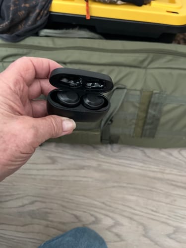 Customer holding the black XCOR Digital Exchange earbuds inside their open charging case, with a tactical bag in the background.