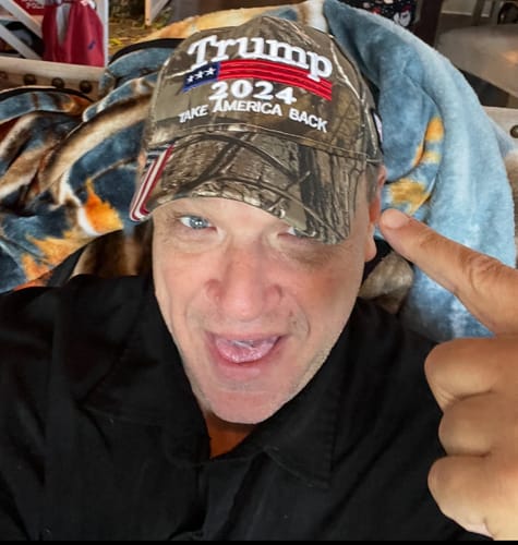 Customer pointing at a camouflage hat embroidered with 'Trump 2024 Take America Back'.