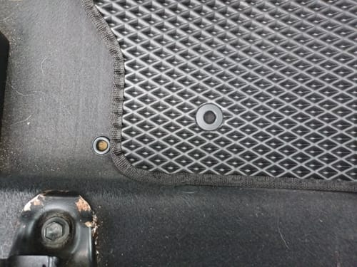 Recenzent pokazuje niedopasowany otwór mocujący w dywaniku samochodowym kierowcy.