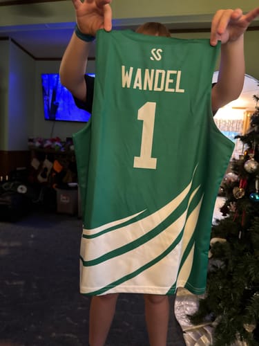 Customer holding up the back of a green and white custom basketball jersey with the name WANDEL and number 1.