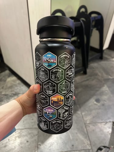 Customer holding their black World Explorer Bottle, decorated with several colorful destination stickers.